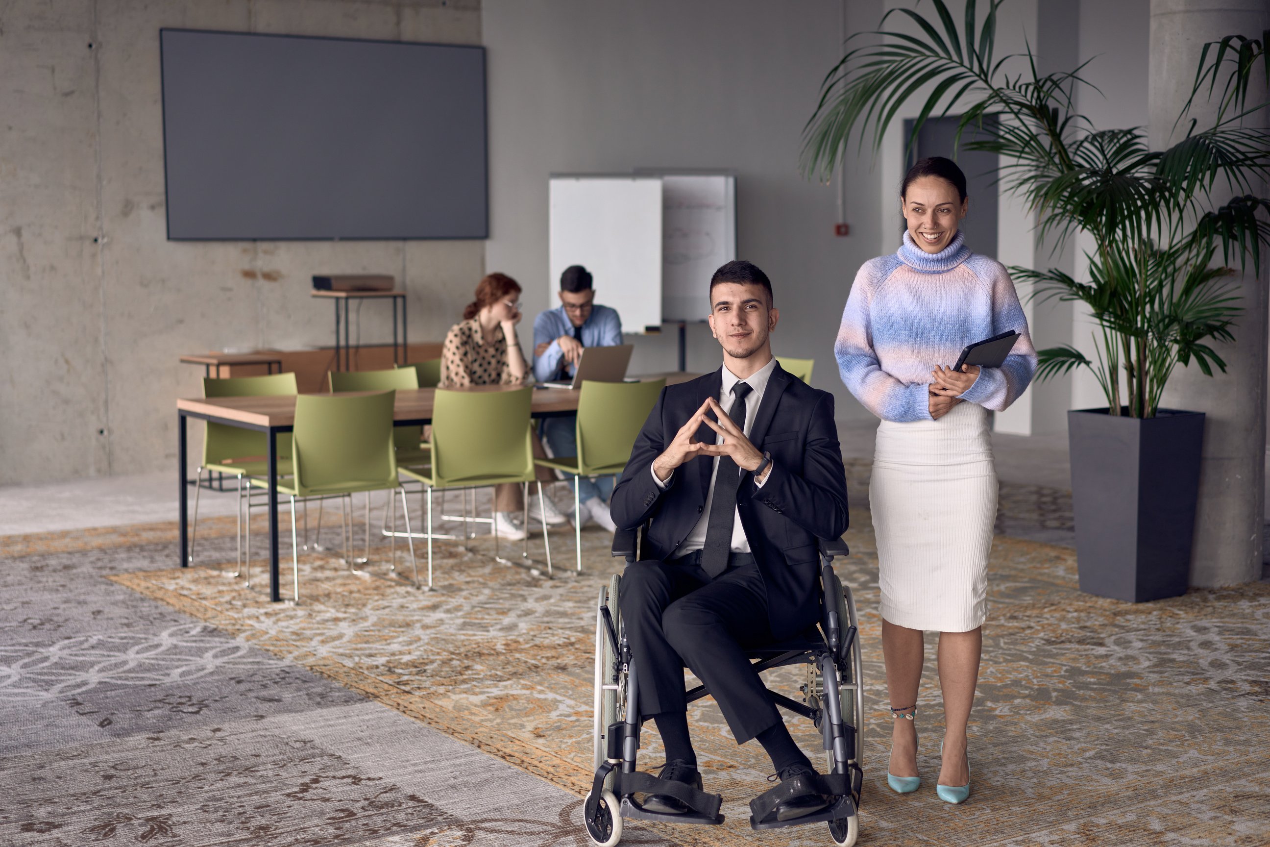 A businessman in a wheelchair and his female colleague together in a modern office, representing the power of teamwork, inclusion and support, fostering a dynamic and inclusive work environment.